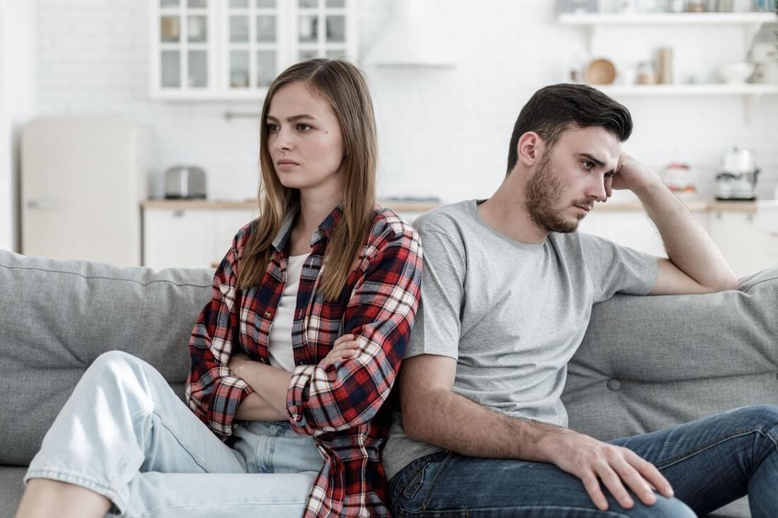 Молодая пара после ссоры сидит на диване, отвернувшись друг от друга