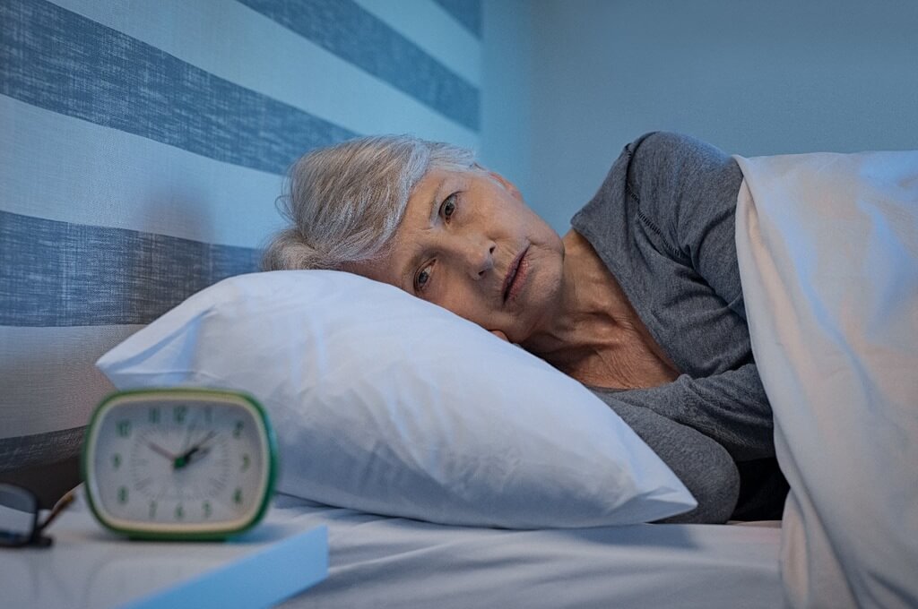 Женщина в возрасте смотрит на будильник и не может уснуть